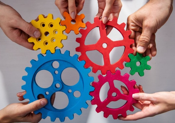 Several hands holding gears that fit together.